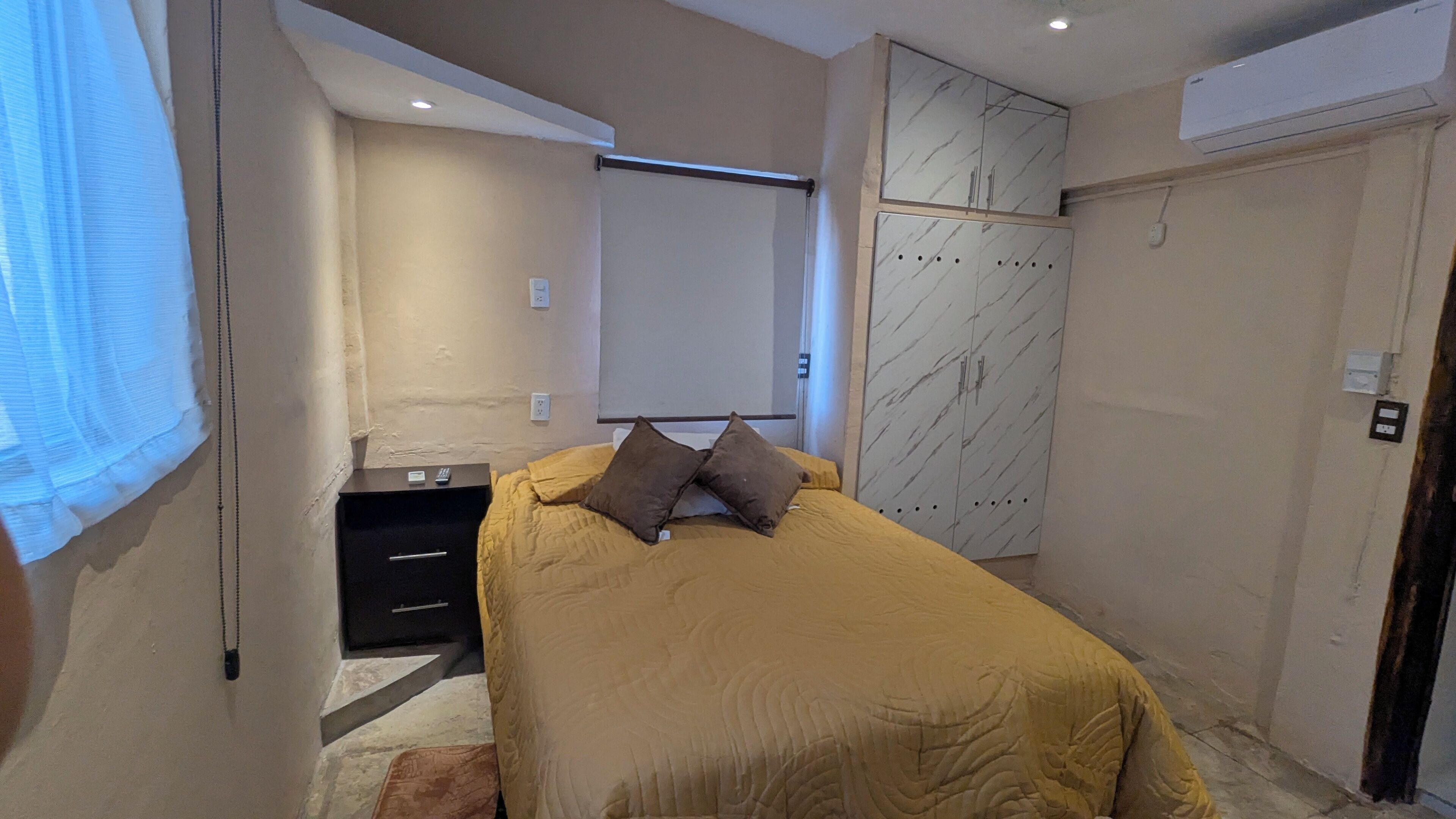 A bedroom with a bed, a nightstand, a wardrobe, and a window with blinds.