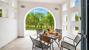 Comedor con una mesa preparada para cuatro personas, rodeada de sillas y vista a zonas verdes a través de un arco.