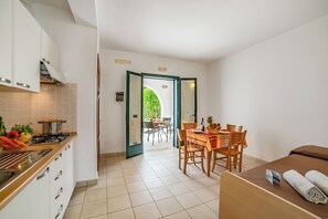 A compact kitchen with a stove, cabinets, and a dining area with a table and chairs. - Beach in 5 min | Pool Access | n.57, Otranto, Italy (Otranto)