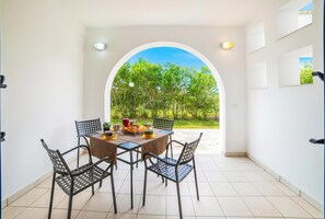 A dining area with a table set for four, surrounded by chairs, and a view of a green landscape through an archway.