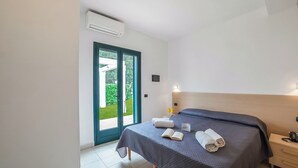 A bedroom with a bed, a bedside table, a nightstand, a window, and an air conditioning unit. - Beach in 5 min | Pool Access | n.51, Otranto, Italy (Otranto)