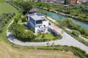 A modern house with a river view, a solar panel on the roof, and a paved driveway.