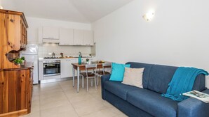 Un espacio habitable compacto con kitchenette, zona de comedor y sofá con manta.