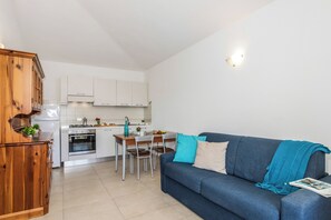 A compact living space with a kitchenette, a dining area, and a sofa with a blanket. - Le Case della Cinta 1 a 300 mt dal mare, San Teodoro, Italy (San Teodoro)