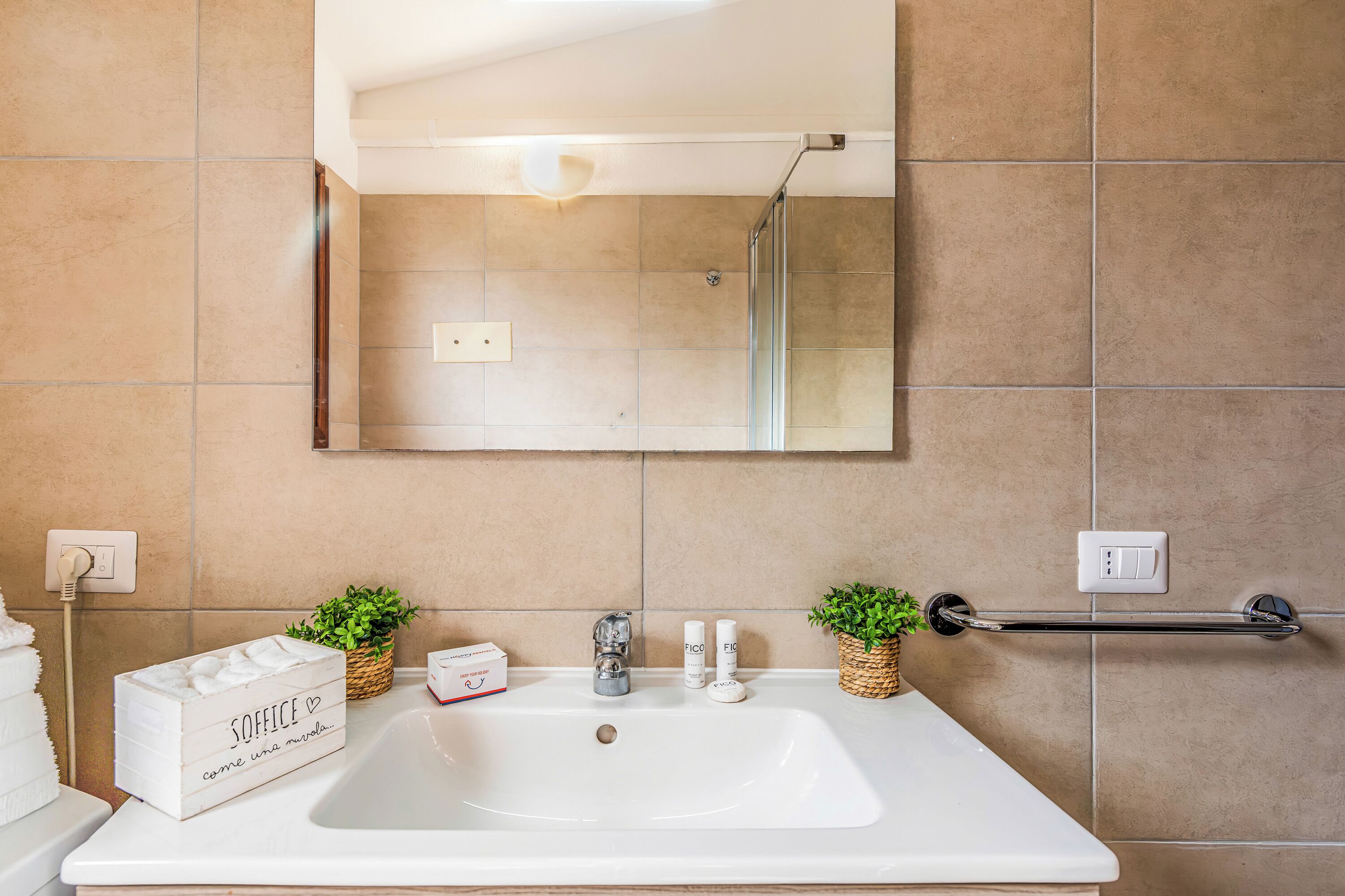 A bathroom with a white sink, two small potted plants, a mirror, and a towel rack.