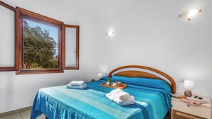 Un dormitorio con cama, mesita de noche, ventana y vistas a árboles.