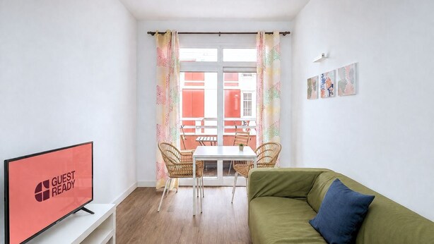 A room with a TV, a green sofa, a dining table with chairs, and a balcony with a view. - GuestReady - Rosamar Playa Canteras II (Las Palmas de Gran Canaria)