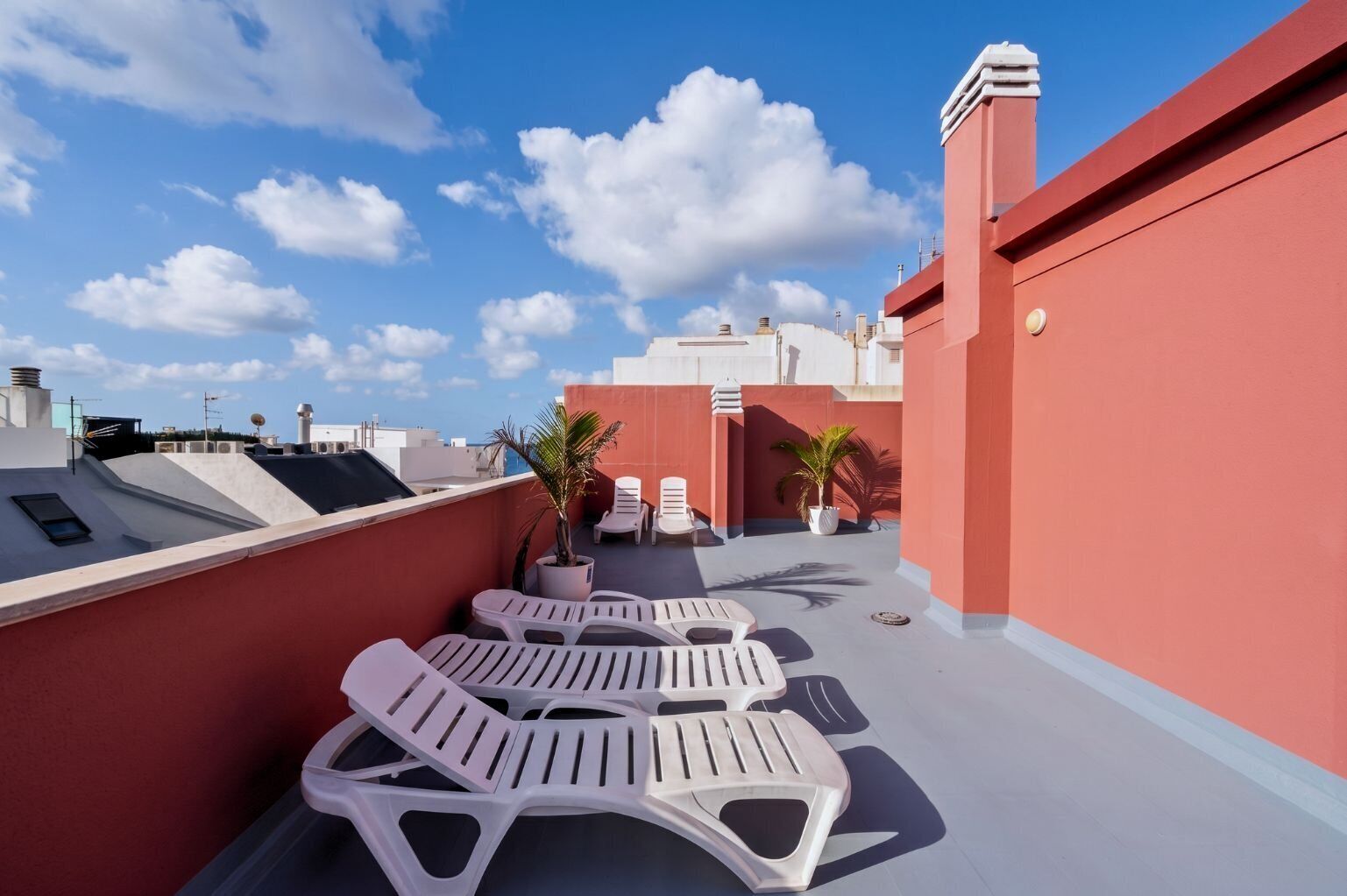 Una terraza en la azotea con sillones blancos, plantas en macetas y un cielo azul despejado.