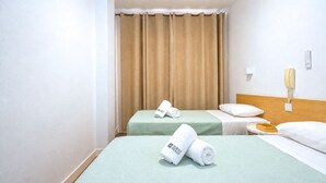 A hotel room with two beds, beige curtains, a bedside table with a lamp, and a wall-mounted phone. - GuestReady - Rosamar Playa Canteras II (Las Palmas de Gran Canaria)