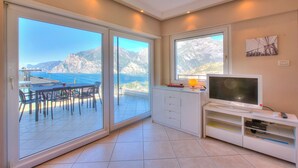 A modern living room with a TV, sliding glass doors to a balcony, and a mountain view.