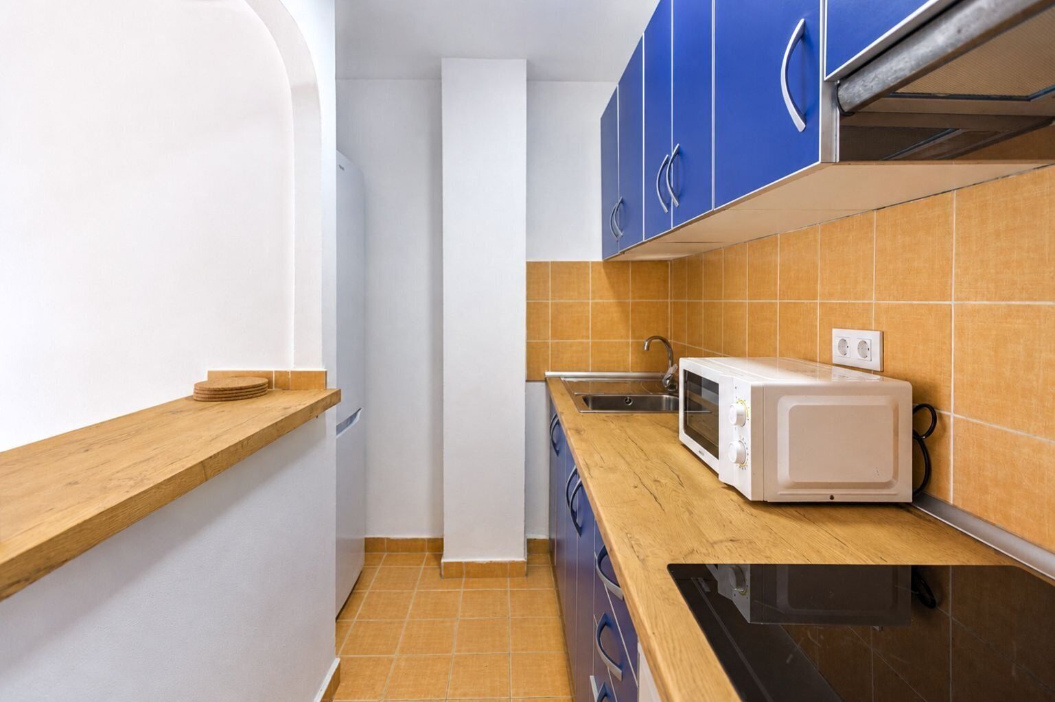 A compact kitchen with a microwave, sink, and wooden countertop.