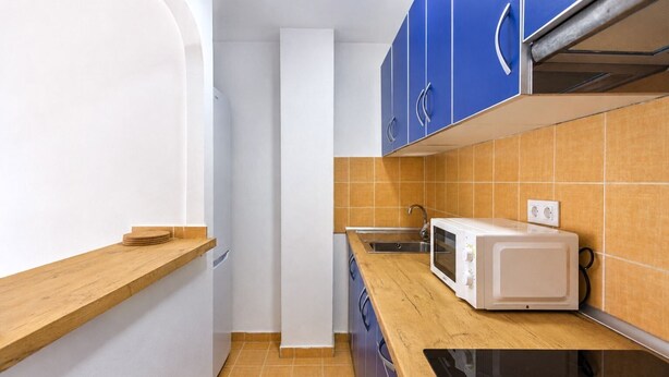 Una cucina compatta con forno a microonde, lavandino e piano di lavoro in legno.