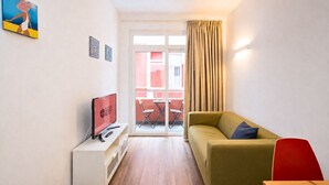 Una camera d'albergo moderna con un divano, una TV, un tavolino e un balcone con vista.