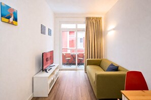 Una habitación de hotel moderna con sofá, televisión, una mesita y balcón con vistas.