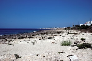 A rocky beach with sparse vegetation, a clear blue sky, and buildings in the distance. - Villino Salentum with Private Pool and Garden, Racale, Italy (Racale)