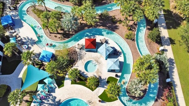 Luchtbeeld van een resort met meerdere zwembaden, ligbedden, parasols en palmbomen.