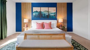 Een slaapkamer met een bed, twee bedlampen, een groot schilderij en een houten bank.