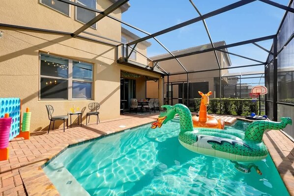 Una piscina esterna con giochi gonfiabili, una zona patio coperta e un canestro da basket.