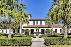 A white building with a tiled roof, a central fountain, and palm trees. - Luxury Villa Game Room, Pool & Resort Access (Kissimmee)
