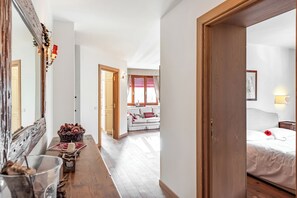 A hallway leading to a bedroom with a bed, a window with curtains, a wooden floor, and a mirror. - Charming Apartment Close to Cableway, Pré-Saint-Didier, Italy (Pré-Saint-Didier)