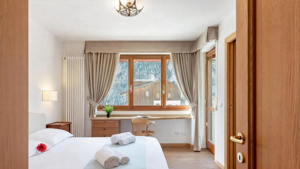 Ein Hotelzimmer mit Bett, Schreibtisch, einem Fenster mit Vorhängen, einer Tür und Blick auf einen Berg.