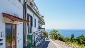 A narrow street with a building on one side, a clear view of the sea, and a stone wall on the other. - Vervece House (Massa Lubrense)