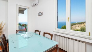 A dining area with a glass table, chairs, a view of the sea, and a white wall with an air conditioner. - Vervece House (Massa Lubrense)