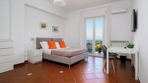 A bedroom with a bed, a desk, a chair, a window with a view, and an air conditioning unit. - Vervece House (Massa Lubrense)