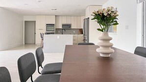 Een moderne keuken met roestvrijstalen apparatuur, een eethoek met een houten tafel en grijze stoelen, en een vaas met bloemen op de tafel.