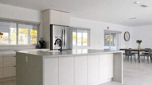 Een moderne keuken met een groot kookeiland, geïntegreerde apparatuur en een eethoek met een klok aan de muur.