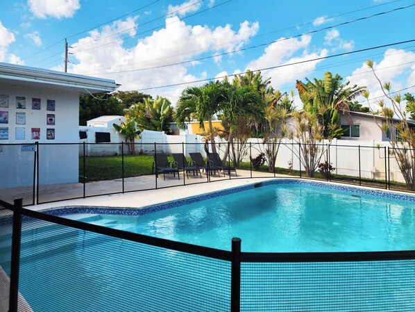 A swimming pool with a tiled edge, surrounded by a fence, and palm trees in the background. - 3-bedroom house in Hollywood with heated pool and large backyard (Hollywood)