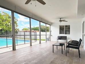 A spacious room with large windows, a ceiling fan, a pool, and a seating area. - 3-bedroom house in Hollywood with heated pool and large backyard (Hollywood)