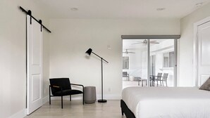 Een slaapkamer met een bed, een stoel, een vloerlamp en uitzicht op een balkon met stoelen.