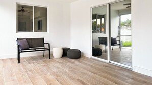 Een kamer met een plafondventilator, een bank, een groot raam en een schuifdeur naar een buitenruimte.