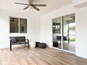 Ein Zimmer mit Deckenventilator, einer Bank, einem großen Fenster und einer Glastür, die zu einem Außenbereich führt.