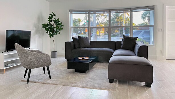 Een moderne woonkamer met een hoekbank, een flatscreen televisie, een potplant en grote ramen.