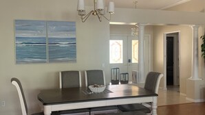 A dining room with a large table, white chairs, a bench, and a chandelier. - Welcome to Coastal Retreat 
at Palo Alto! (The Villages)