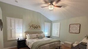 A bedroom with a bed, nightstands, a ceiling fan, and a window with shutters. - Welcome to Coastal Retreat 
at Palo Alto! (The Villages)