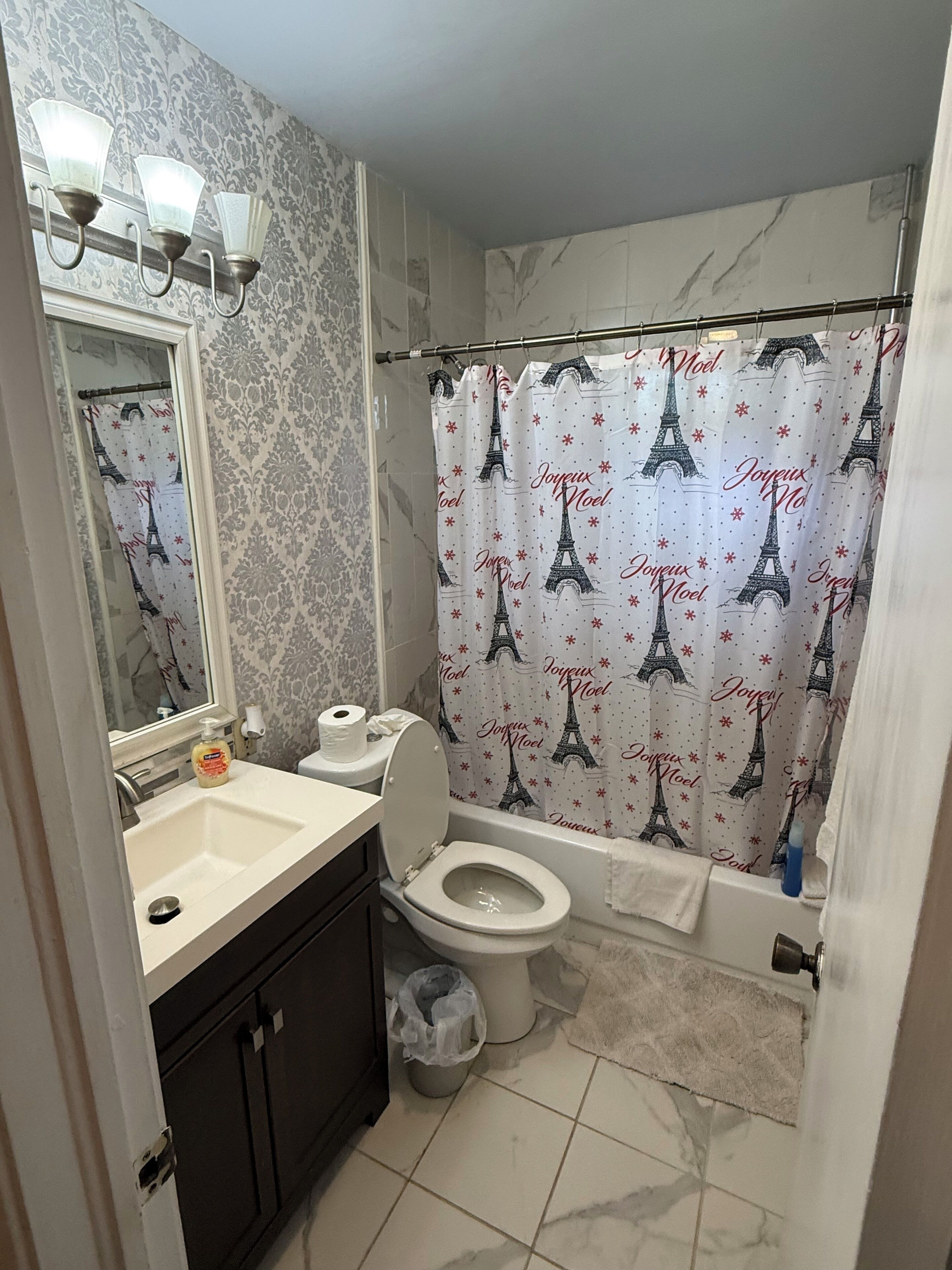 A bathroom with a toilet, sink, mirror, and shower curtain with Eiffel Tower design.