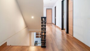 Un corridoio moderno di un hotel con pavimento in legno, una scala e una libreria.