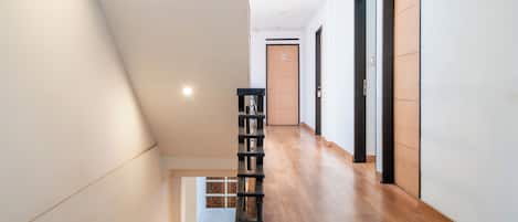 Un pasillo moderno de hotel con piso de madera, una escalera y una estantería.