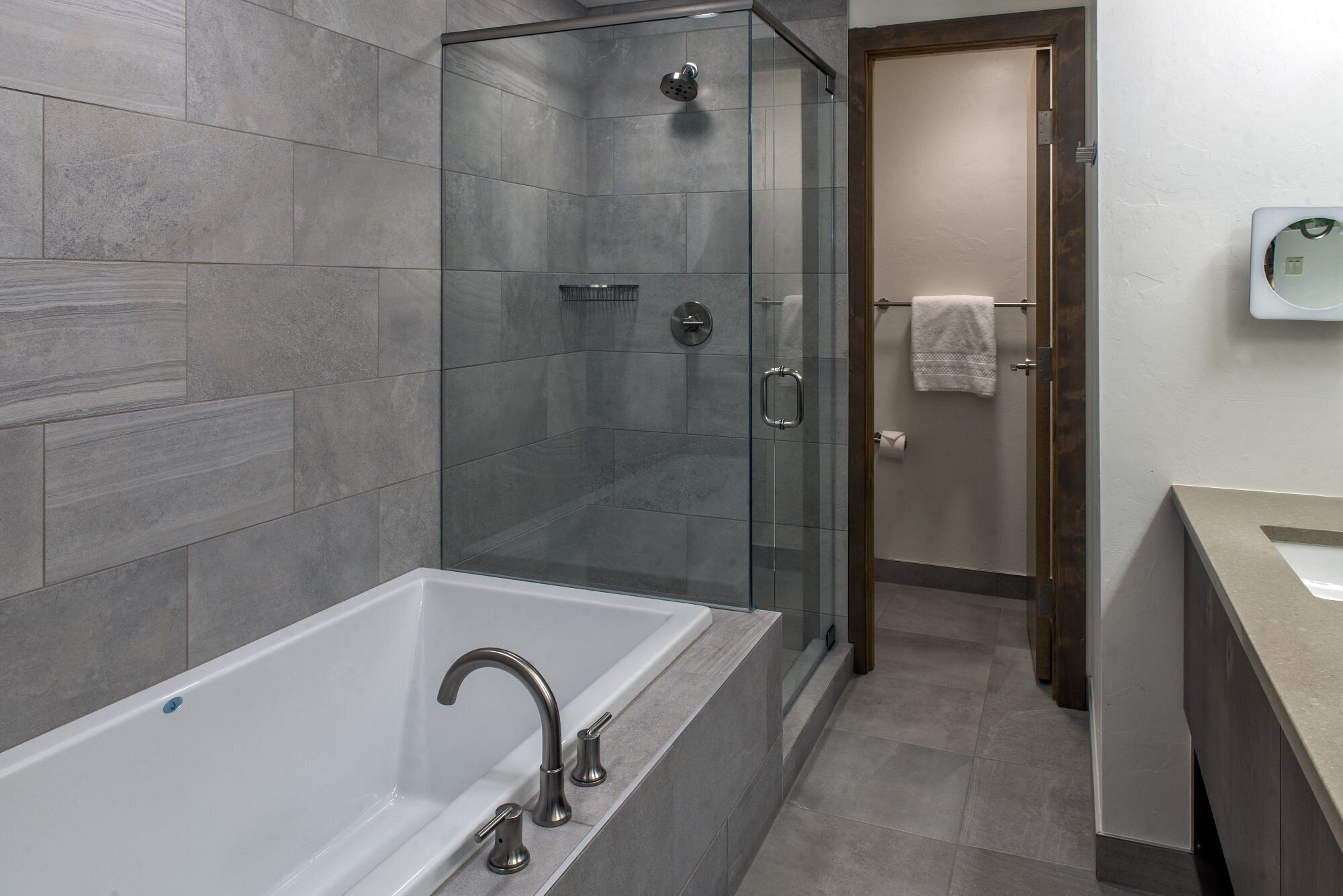 Un baño moderno con ducha envuelta en cristal, una bañera blanca y una puerta de madera.