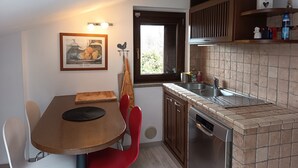 A compact kitchen with a dining table, red chairs, a dishwasher, and a window with a view.