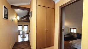 A hallway with wooden flooring, a wooden wardrobe, a dining area with chairs and a table, and a bedroom with a bed and a chair.