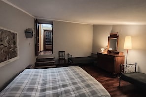 Ett sovrum med en säng, en byrå, en stol, ett skrivbord, en lampa och en trappa som leder ut till ett utomhusområde.