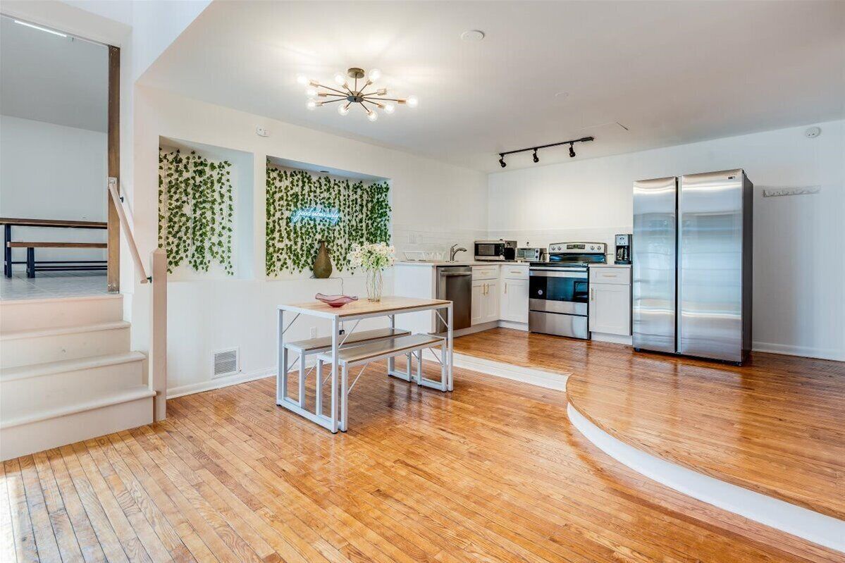 A modern kitchen with stainless steel appliances, a wooden floor, and a staircase leading to an upper level.
