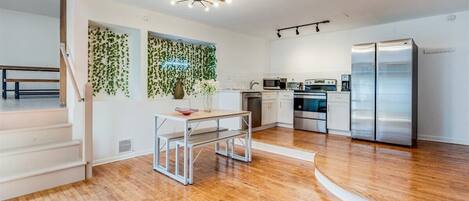 A modern kitchen with stainless steel appliances, a wooden floor, and a staircase leading to an upper level.
