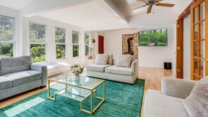 A spacious living room with a ceiling fan, large windows, a stone fireplace, and a green carpet. - !Poconos Hidden Villa de’Casablanca Pool+Spa Creek (Stroudsburg)