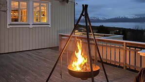A deck with a fire pit in the center, a wooden railing, and a view of mountains and a lake. - Amazing home in Sømna with WiFi (Sømna)