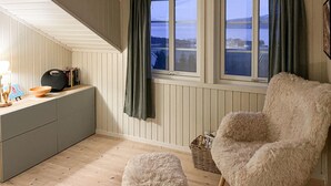 A cozy room with a wooden ceiling, a window with curtains, a fluffy chair, a small table with books and a lamp, and a wooden floor. - Amazing home in Sømna with WiFi (Sømna)